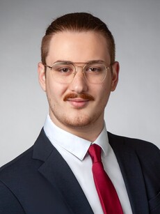 Person in Anzug mit roter Krawatte vor grauem Hintergrund.